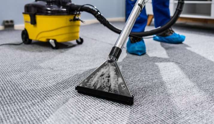 image of a cleaner wearing shoe coverings hoovering the carpet
