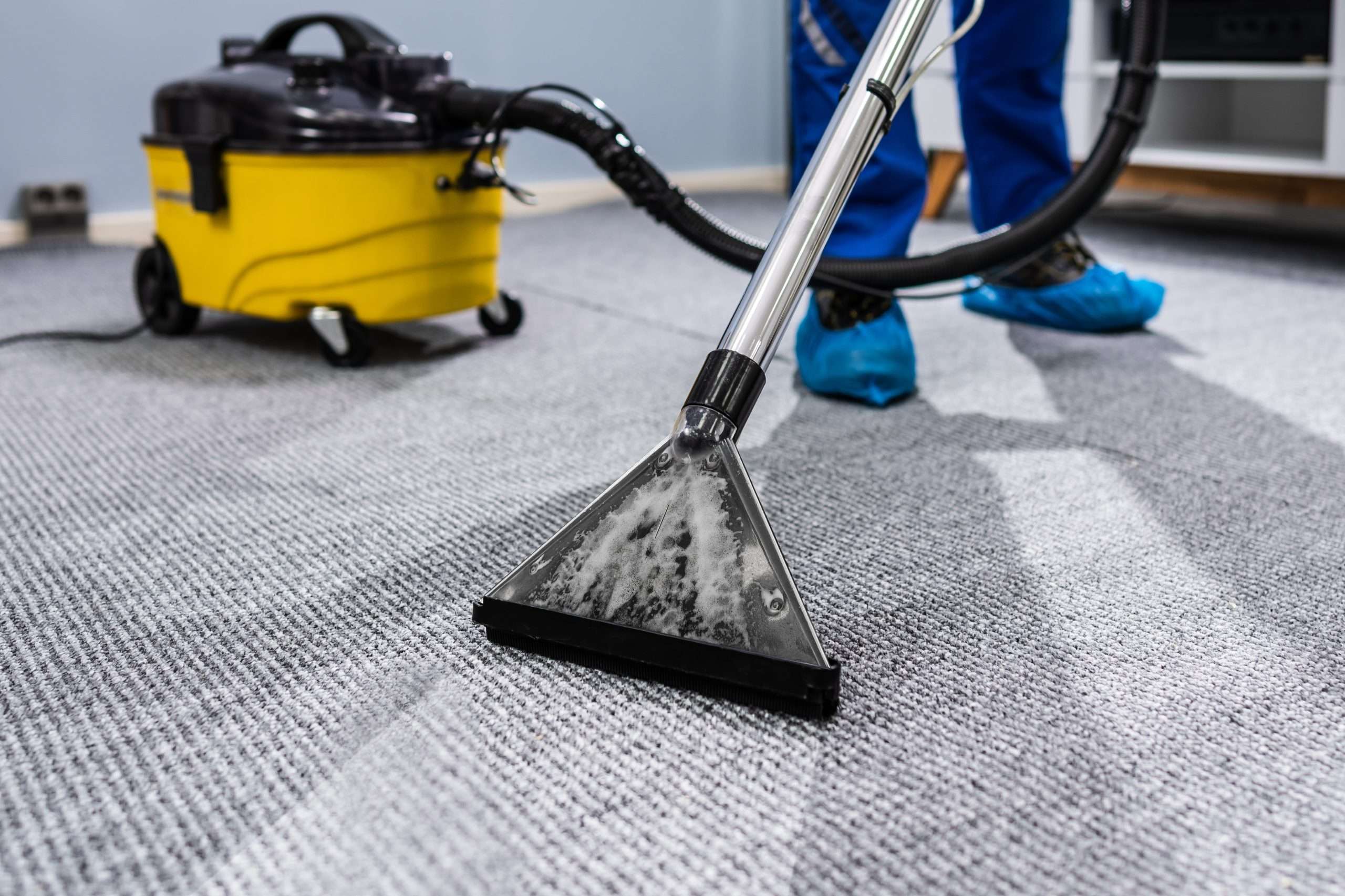 image of a cleaner wearing shoe coverings hoovering the carpet