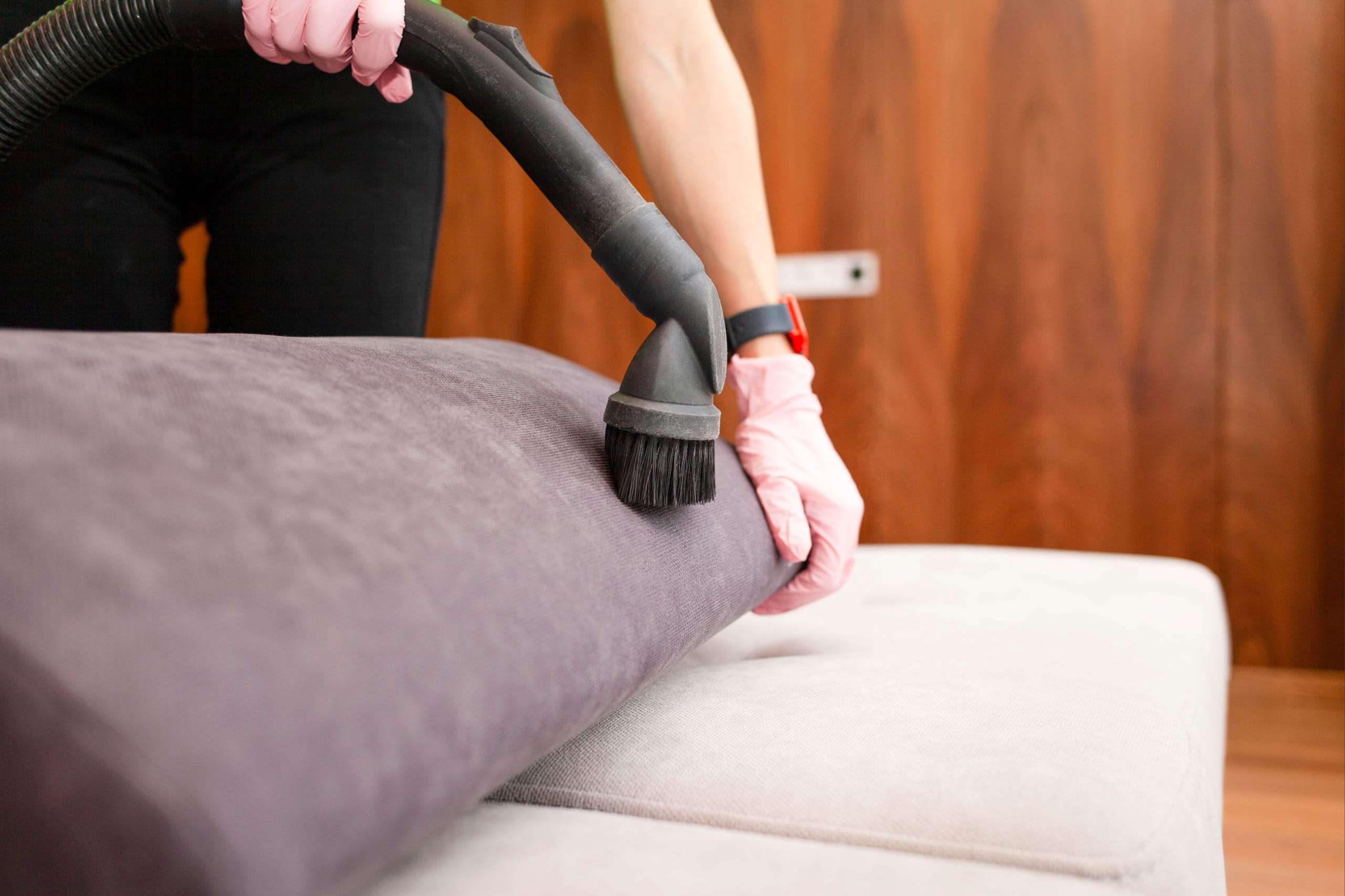 person cleaning the sofa wearing pink gloves and holing a hoover