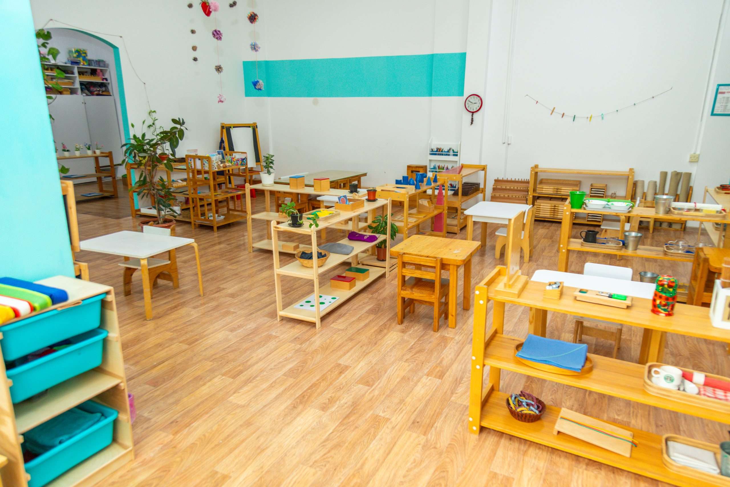 A colorful clean nursery classroom with wooden furniture and educational materials. Plants and decorations create a welcoming environment.